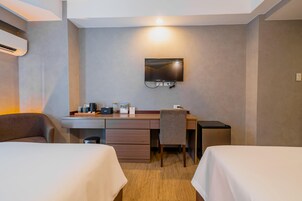 Quarto de hotel com duas camas, uma escrivaninha com televisão de tela plana, uma cadeira, uma mesa pequena e um minibar.