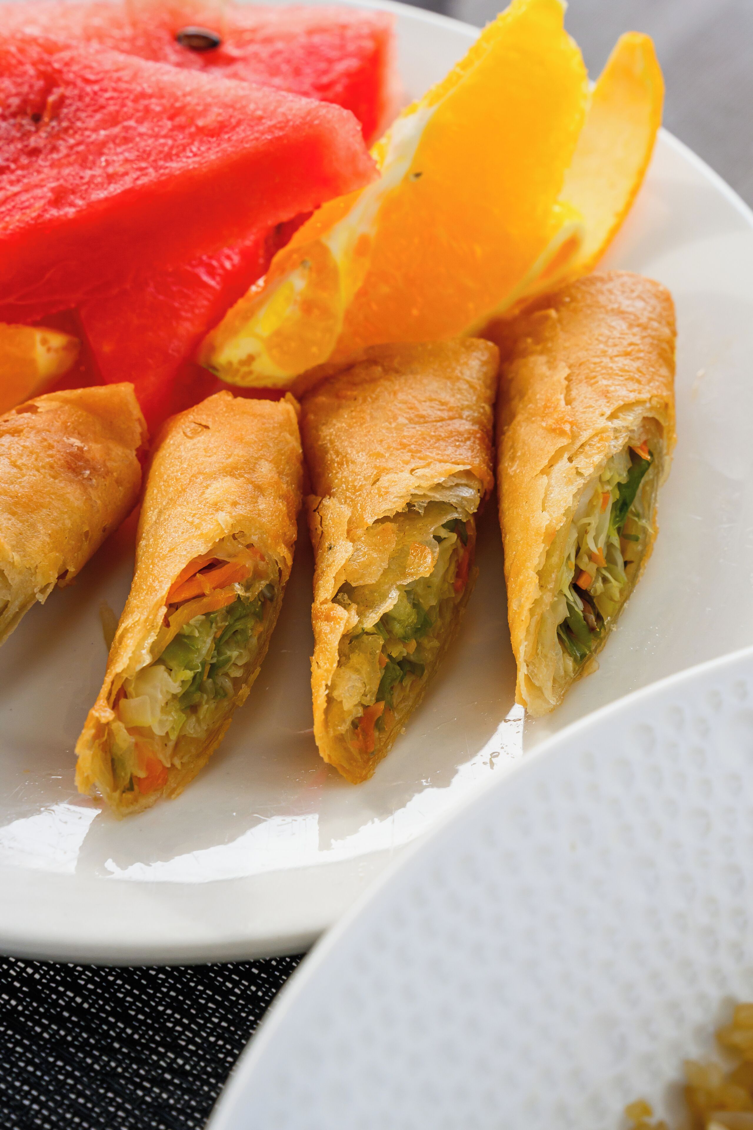 A plate with spring rolls, watermelon, and an orange slice.