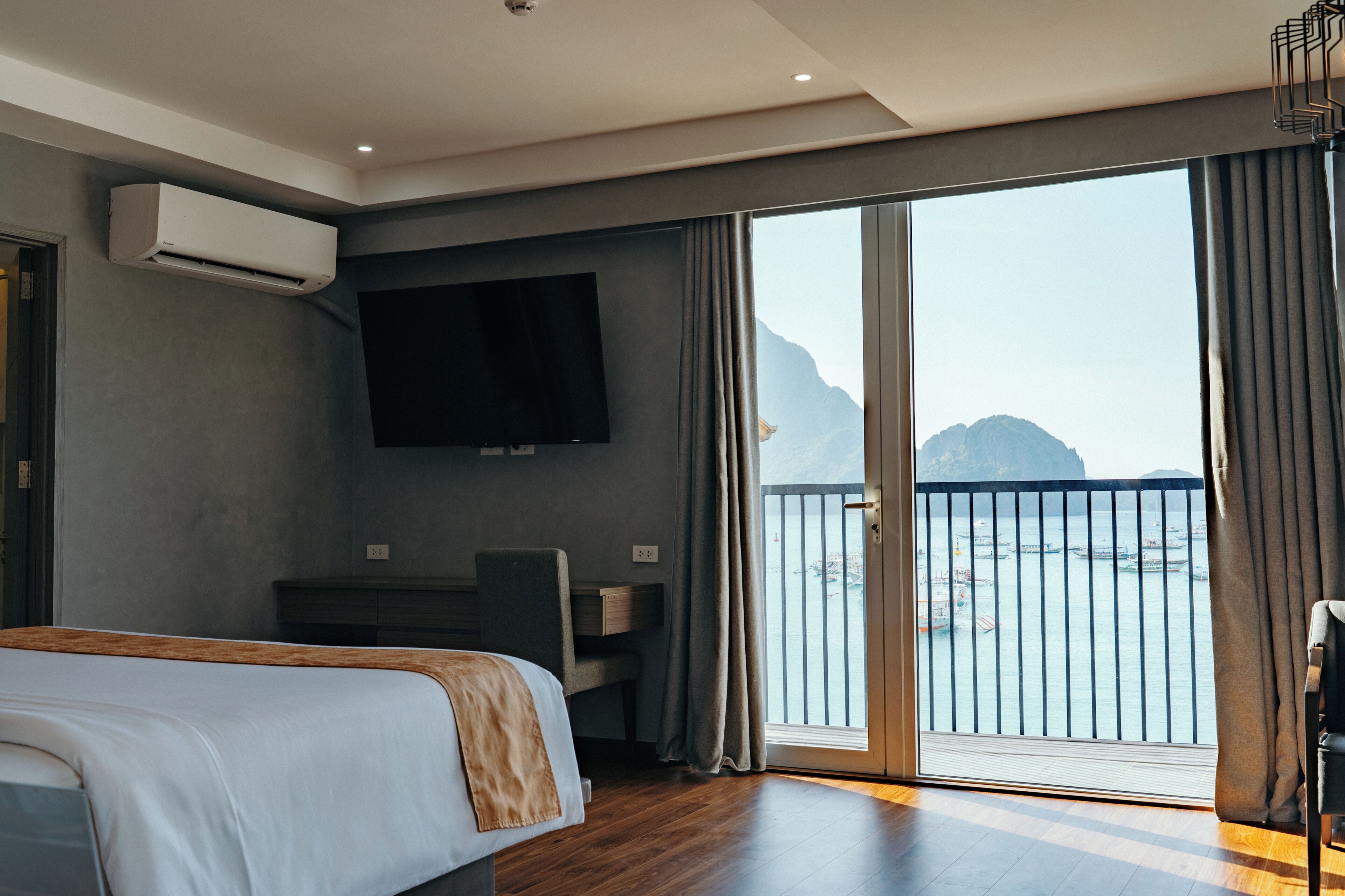 A hotel room with a bed, a desk, a TV, and a balcony with a view of the sea.