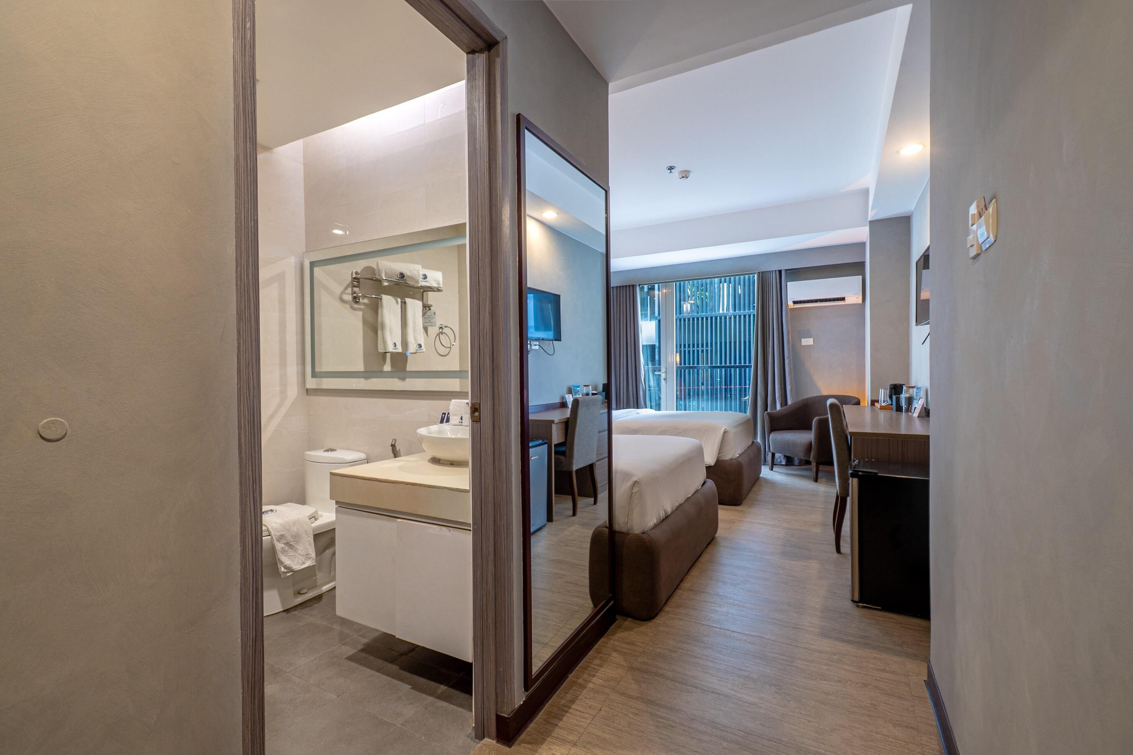 A modern hotel room with a bathroom, a bed, a desk, and a view of the outside.