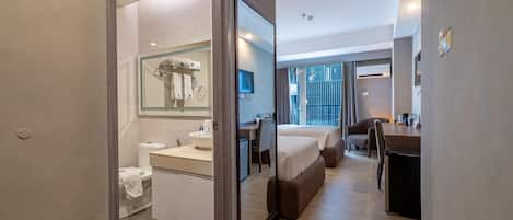 A modern hotel room with a bathroom, a bed, a desk, and a view of the outside.