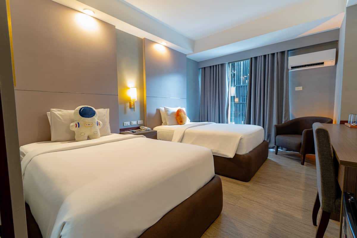 A hotel room with two beds, a desk, a chair, and an air conditioning unit.