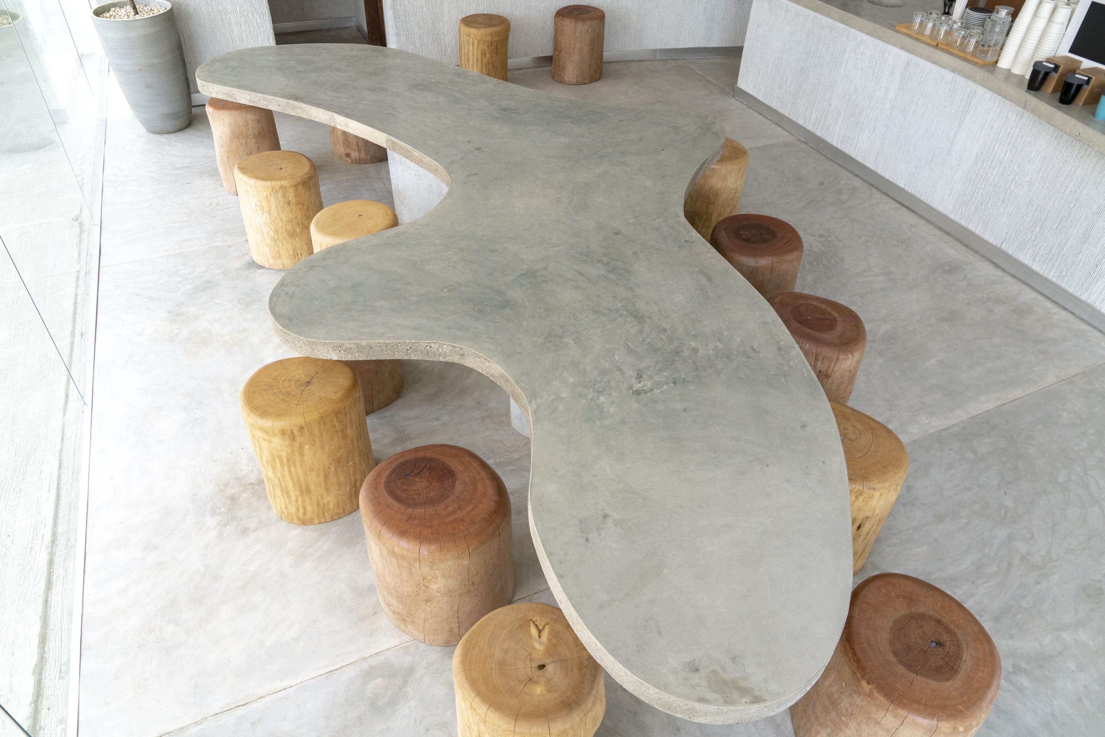 Un tavolo in pietra dalla forma particolare, curvo, circondato da sgabelli di legno in un ambiente moderno.