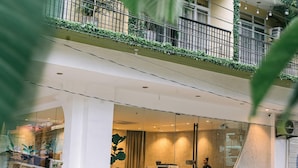 A building with a glass facade, a reception area, and a balcony with greenery.