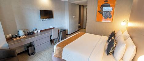A hotel room with a bed, desk, chair, TV, and artwork.