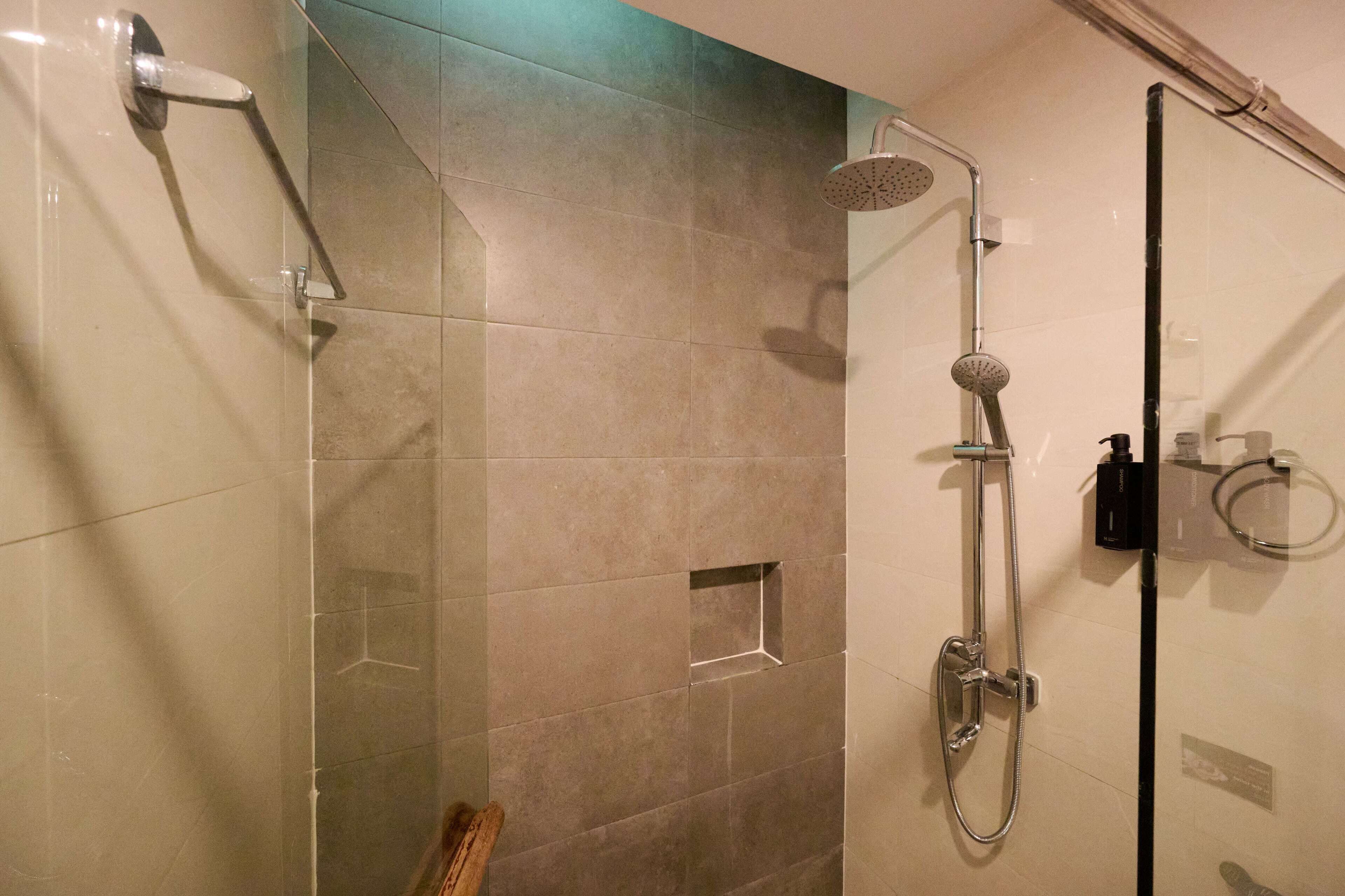 A glass-enclosed shower with a handheld showerhead and a wall-mounted rain showerhead.