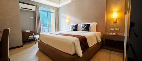 Une chambre d’hôtel avec un grand lit, un bureau, une chaise, un balcon et une lampe fixée au mur.