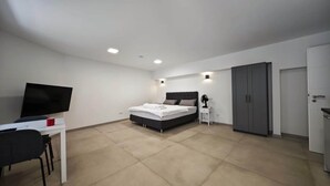 A bedroom with a bed, a desk with a TV, a wardrobe, and a small bedside table with a fan. - Residence Studio Nr.5 (Badenweiler)