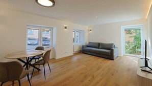 Una sala moderna con un sofá gris, una mesa de comedor con sillas y un televisor sobre un mueble.