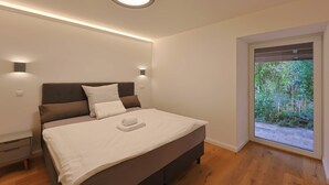 Un dormitorio con cama, mesitas de noche, una lámpara de techo y una ventana con vistas a zonas verdes.