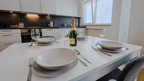 Eine moderne Küche mit weißen Schränken, einer schwarzen Arbeitsplatte und einem Essbereich, gedeckt mit Tellern, Besteck und einer Champagnerflasche.