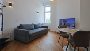 Een moderne woonkamer met een grijze bank, een eettafel met stoelen, een televisie en een groot raam met uitzicht.