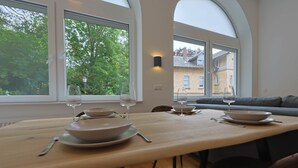 A dining area with a long table set for two, large windows, and a view of a residential building. - Deluxe Apartment No.03 with 2 bedrooms (Badenweiler)