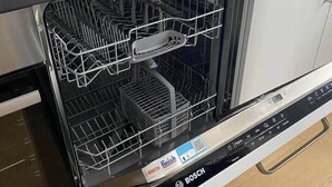 Un lavavajillas Bosch con un panel de control, una rejilla para platos y una botella de detergente Fairy sobre la encimera.