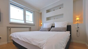 Un dormitorio moderno con una cama grande, estanterías empotradas, un radiador y una ventana con persianas.