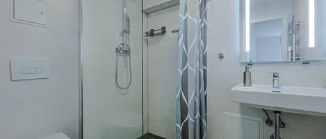 A modern bathroom with a glass shower enclosure, a white toilet, a sink with a mirror, and a shower curtain with a geometric pattern.