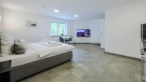 Quarto de hotel moderno com cama, escrivaninha, cadeira, televisão e janela.
