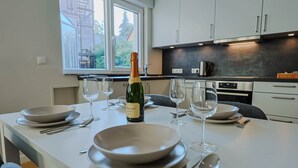 Una cocina moderna con armarios blancos, un ventanal grande y una mesa de comedor con copas de vino, platos y cubiertos.