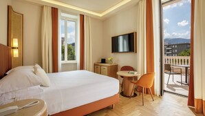 A hotel room with a large bed, a bedside table with a phone, a desk with a chair, a TV mounted on the wall, and a balcony with outdoor seating. - Villa Miliani (Fabriano)