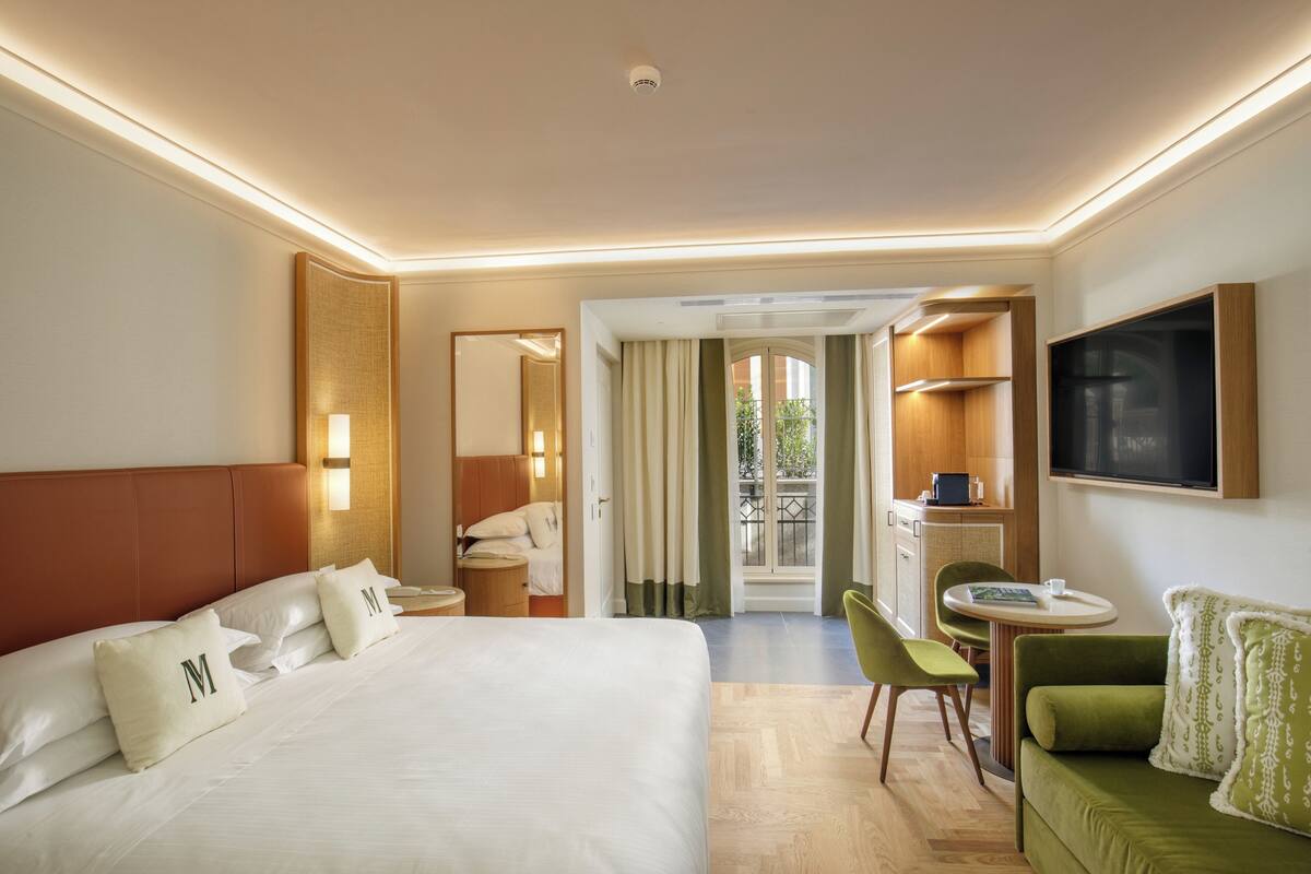 A hotel room with a large bed, a green sofa, a dining table, and a TV.