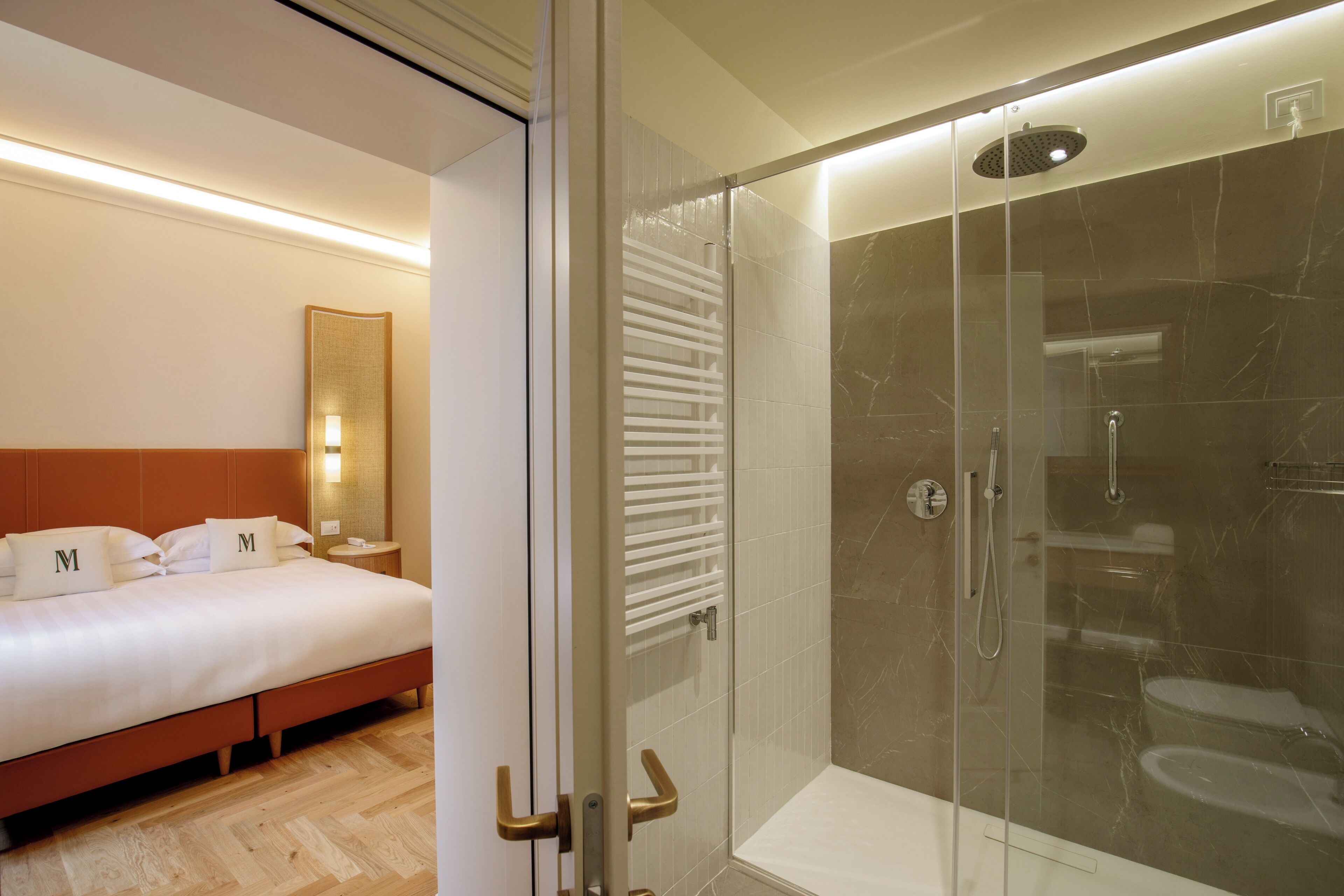 A hotel room with a bed, a glass-enclosed shower, and a bedside table with a lamp.