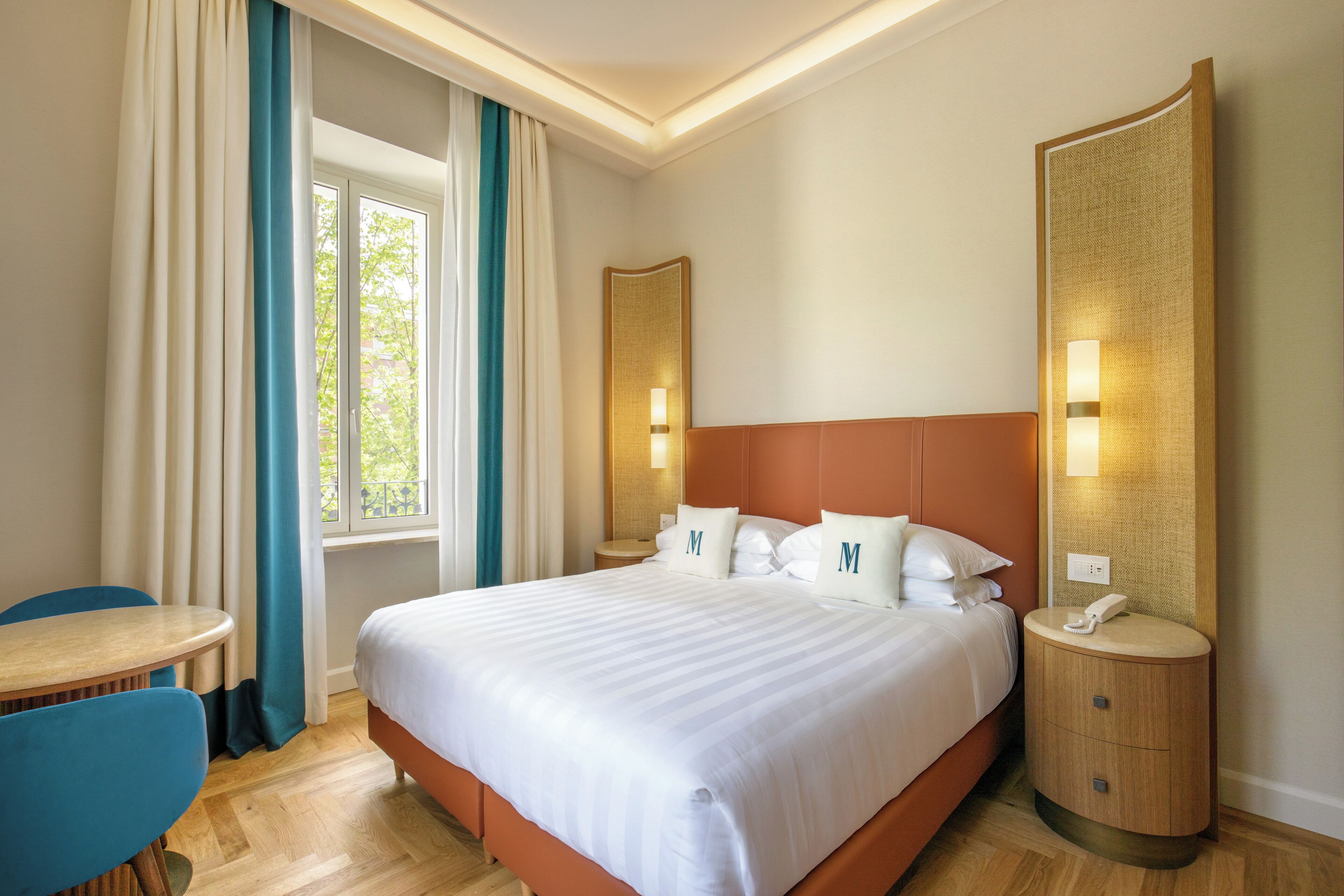 A hotel room with a large bed, a bedside table, a chair, and a window with curtains.