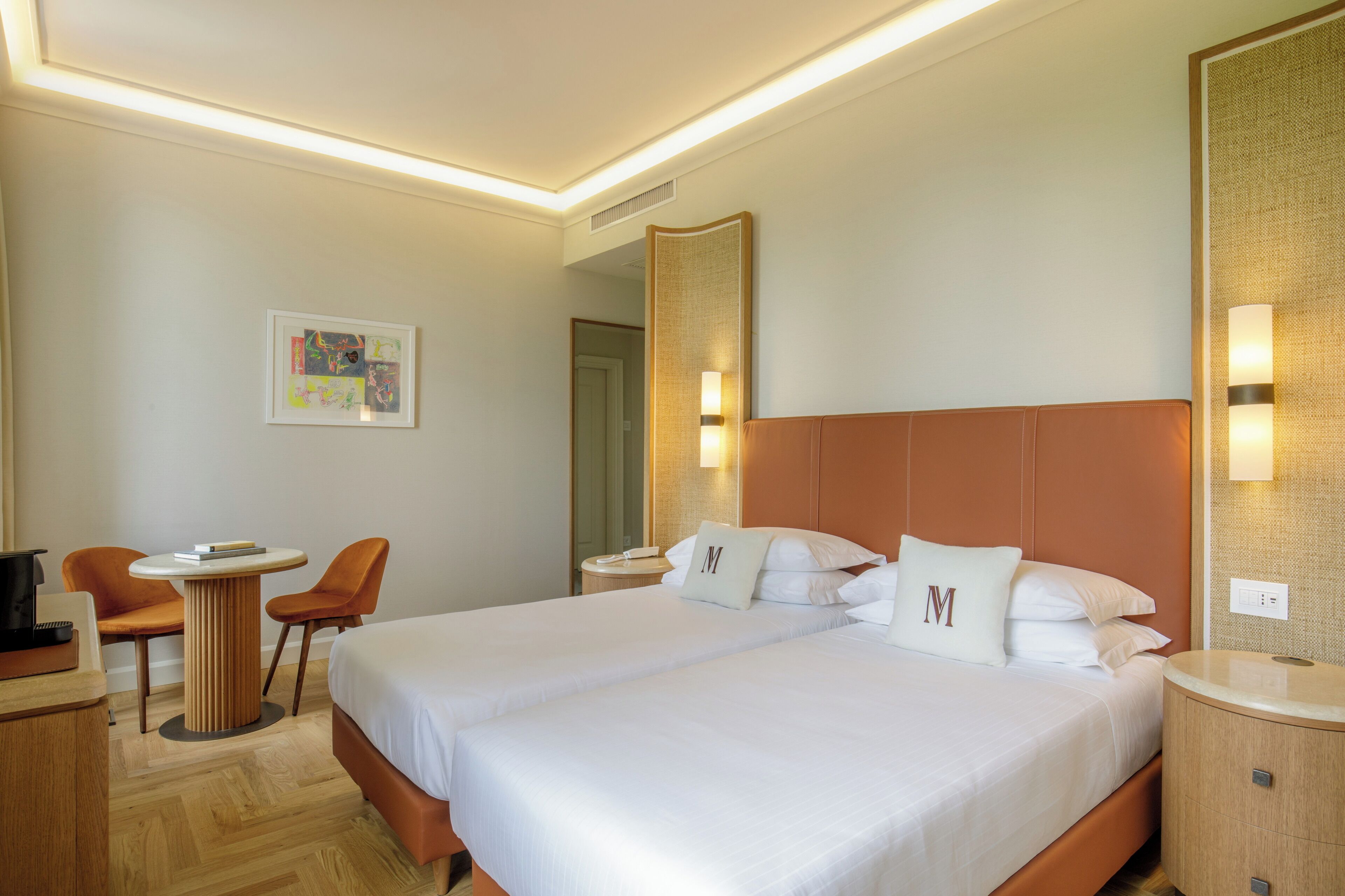 A hotel room with two beds, a desk, chairs, and a large mirror.