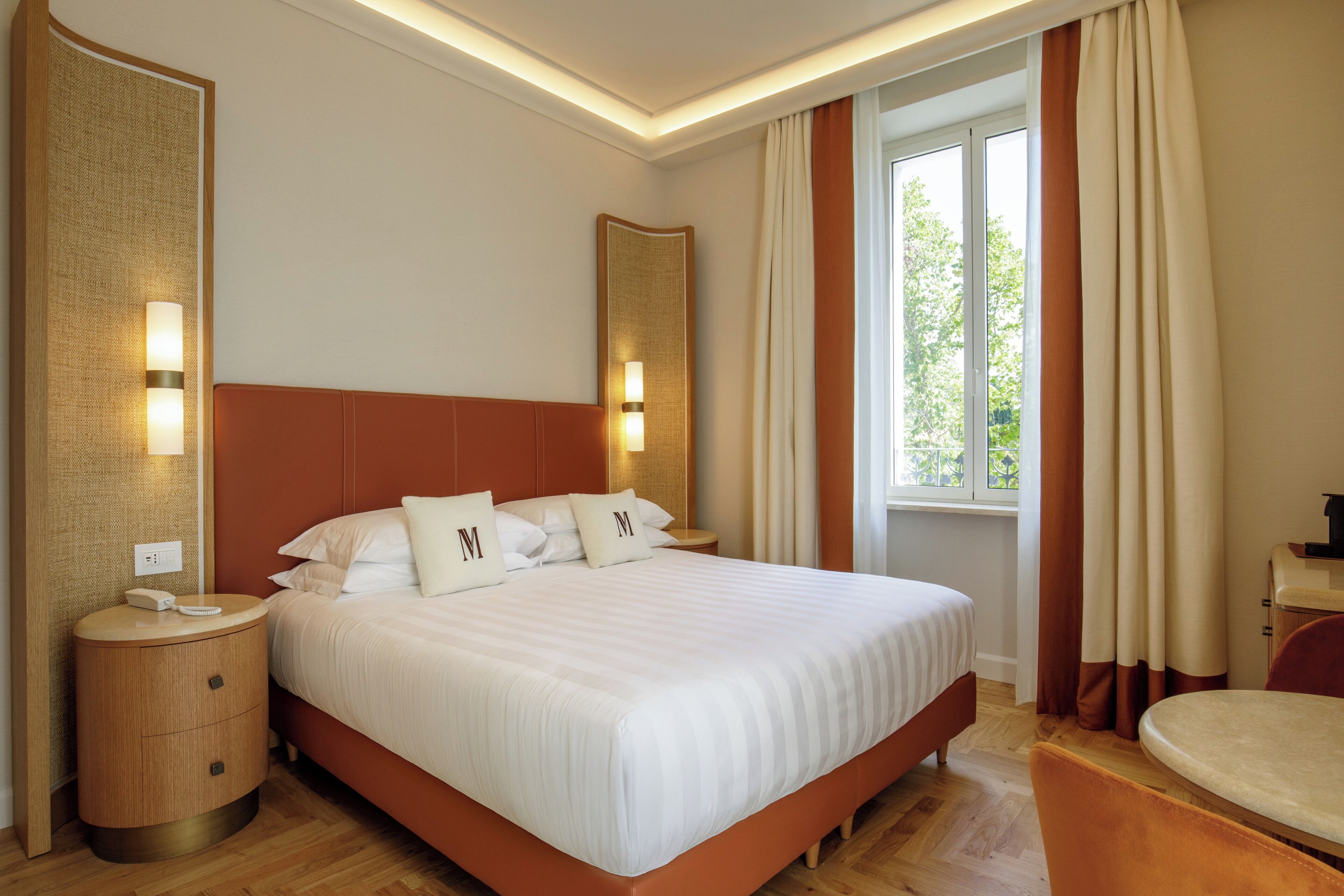 A hotel room with a large bed, bedside lamps, a nightstand, a window with curtains, and a small table.