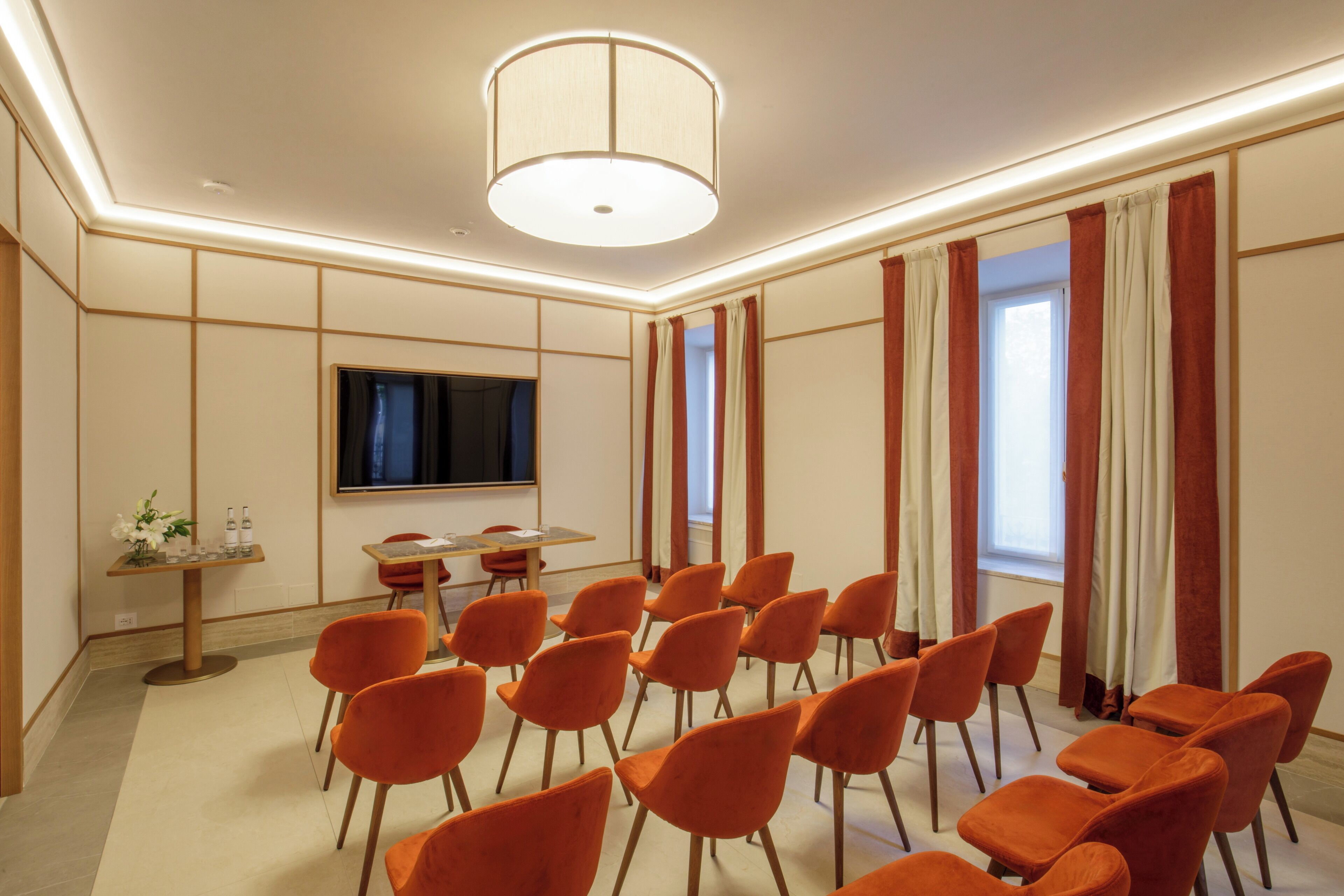 A conference room with orange chairs, a large flat-screen TV, and a table with a vase of flowers.