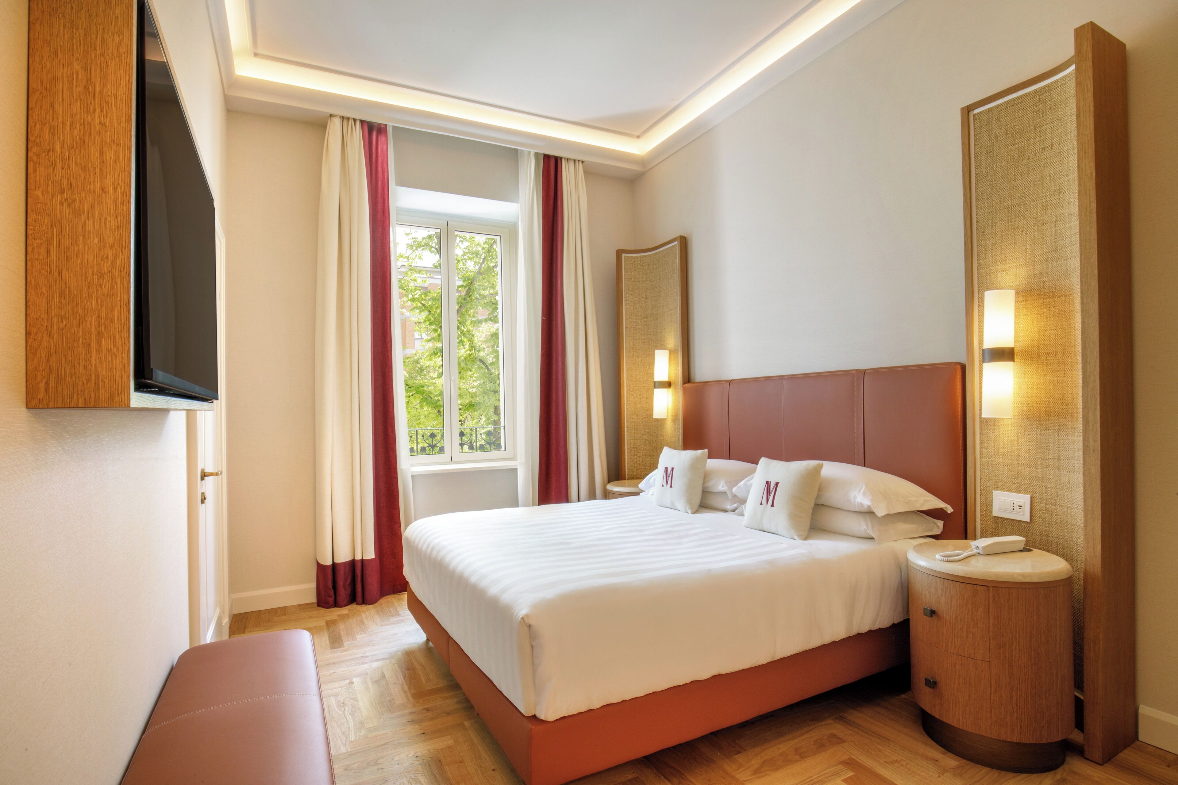 A hotel room with a large bed, a bedside table with a phone, a mirror, and a window with curtains.