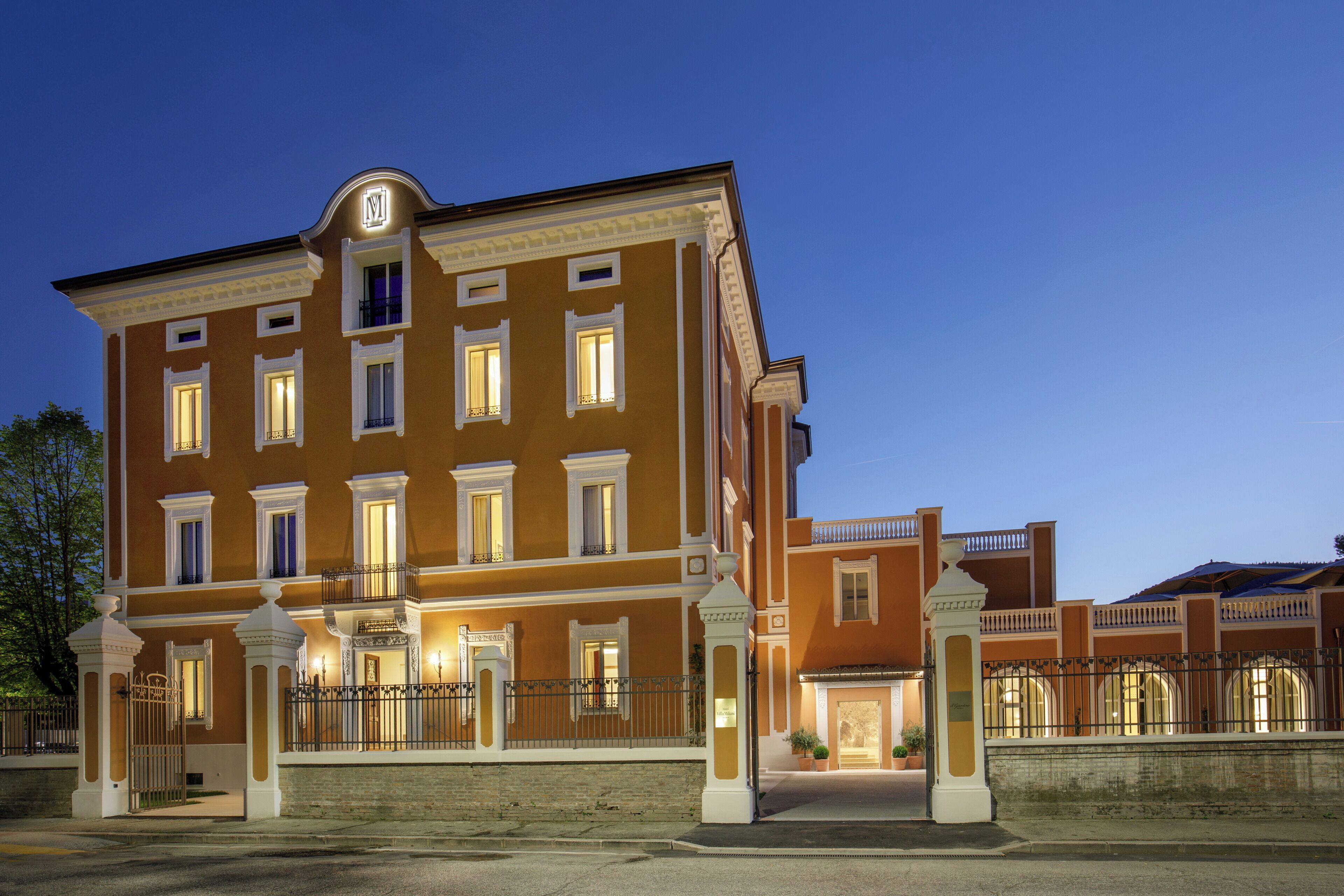 A large, multi-story building with a symmetrical facade, multiple balconies, and a prominent entrance with a gated driveway.