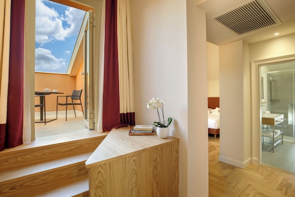 A modern hotel room with a wooden desk, a small potted plant, and a view of the sky through an open window.
