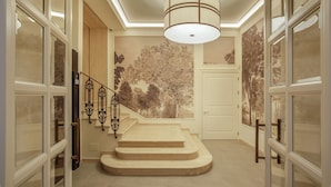 A grand staircase with a decorative railing, a large wall mural, and a modern ceiling light fixture. - Villa Miliani (Fabriano)