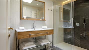 Un baño moderno con cabina de ducha de vidrio, tocador de madera con espejo y repisa de vidrio con toallas.