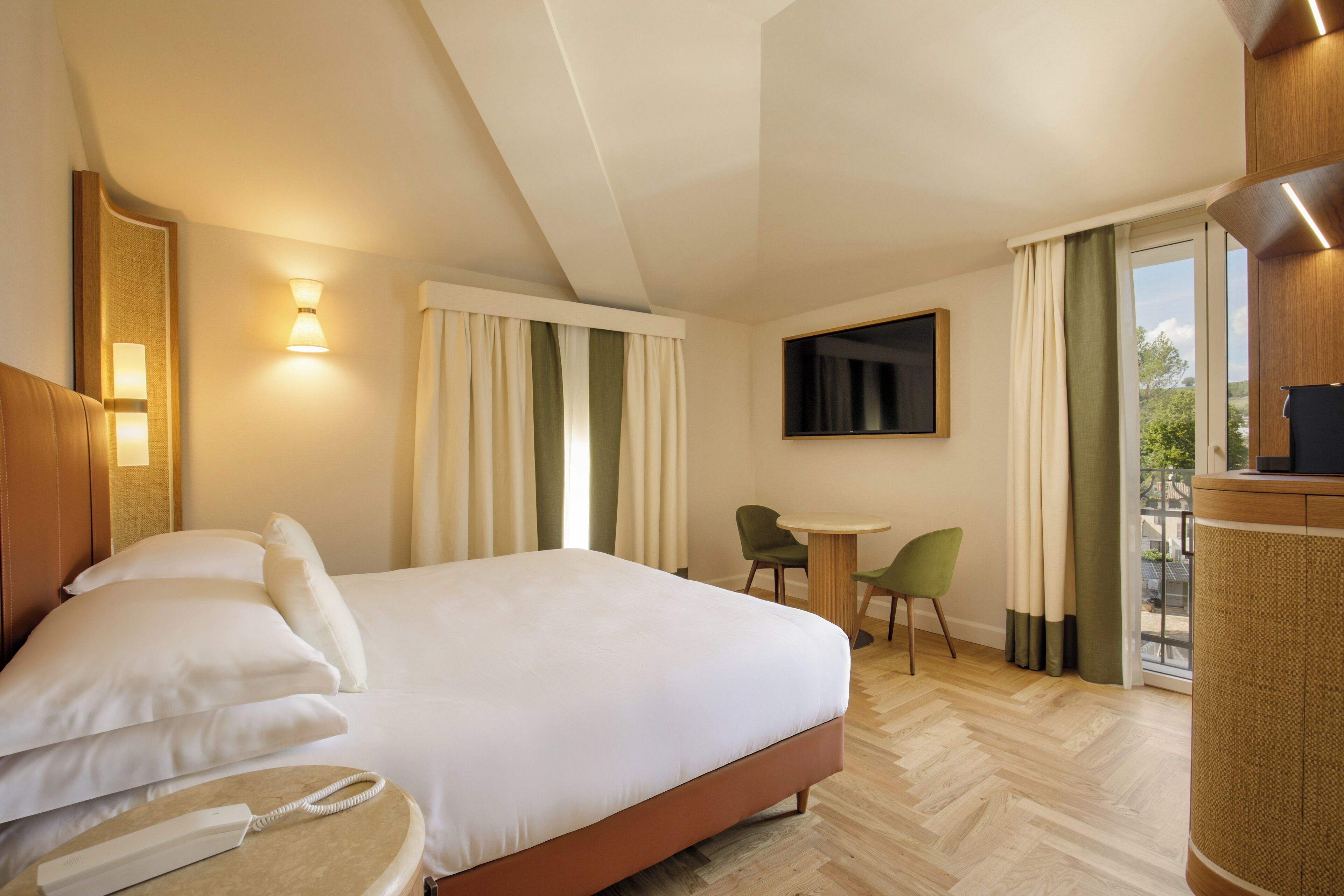 A hotel room with a large bed, a desk, a chair, a television, and a balcony with curtains.