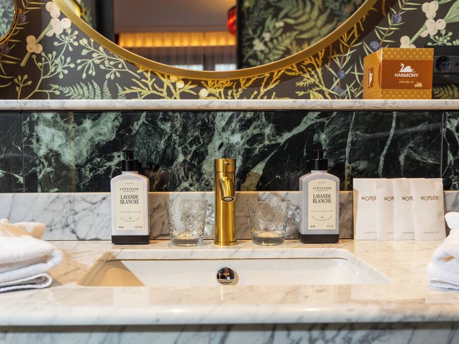 A bathroom vanity with a marble sink, gold faucet, and toiletries.