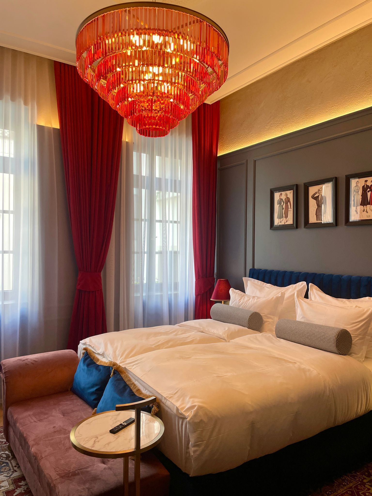 A hotel room with a large bed, a red chandelier, a sofa, and a small table.