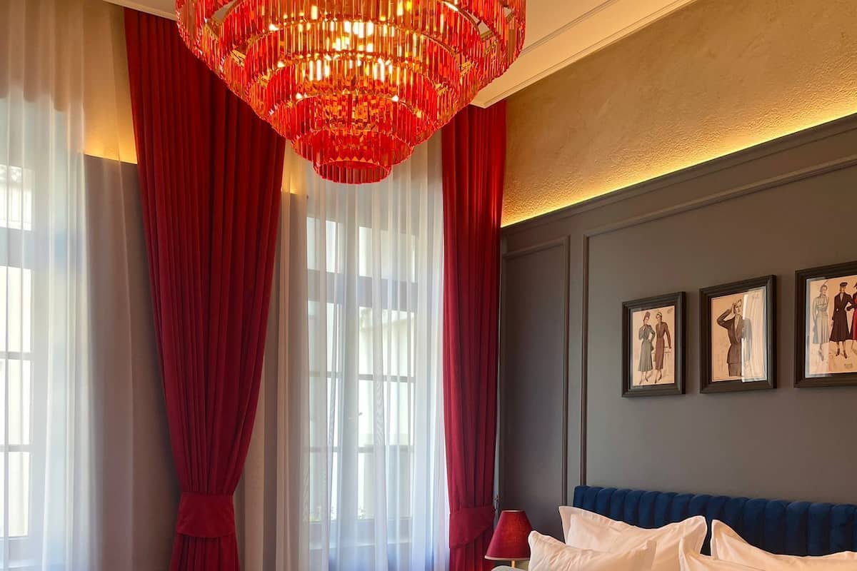 A hotel room with a large bed, a red chandelier, a sofa, and a small table.
