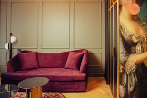 A room with a red velvet sofa, a small round table, and a painting of a woman blowing a bubble.