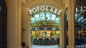 Una hall d'albergo con un'area bar centrale chiamata 'Popolare', caratterizzata da un pavimento a motivi geometrici e un soffitto a volta.