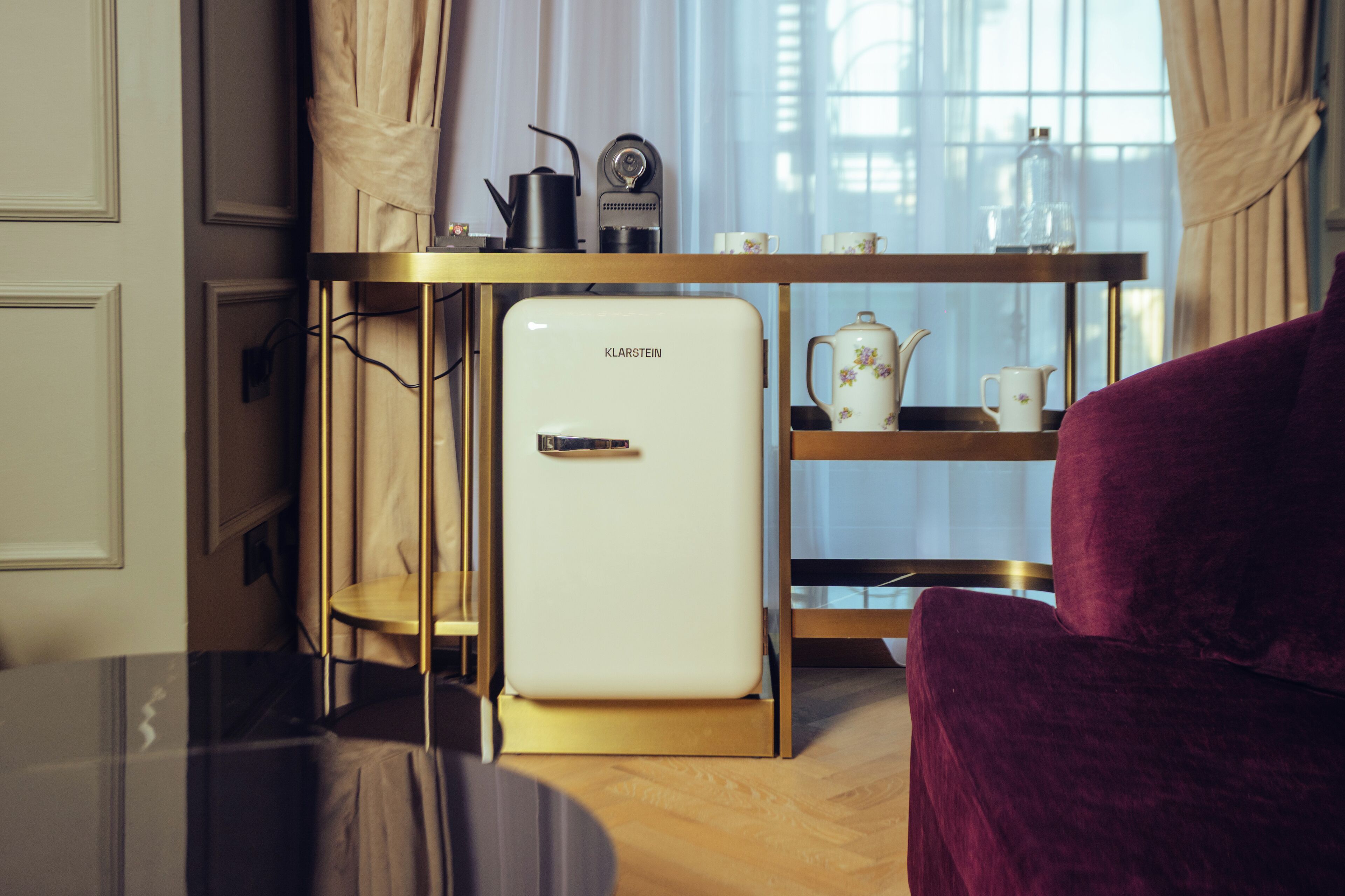 Una kitchenette compacta con un refrigerador blanco, una cafetera y un hervidor sobre una mesa de madera.