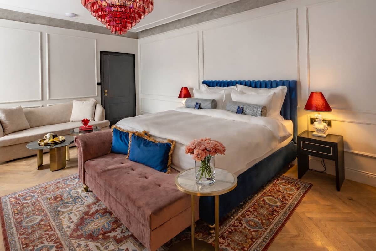 A bedroom with a large bed, a sofa, a coffee table, a nightstand, a lamp, and a chandelier.
