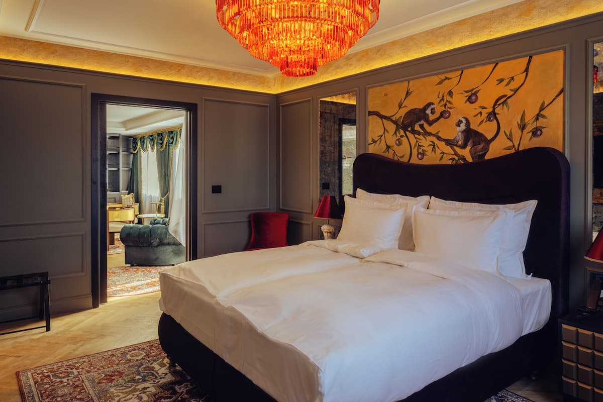 A spacious bedroom with a large bed, a chandelier, and a wall mural.