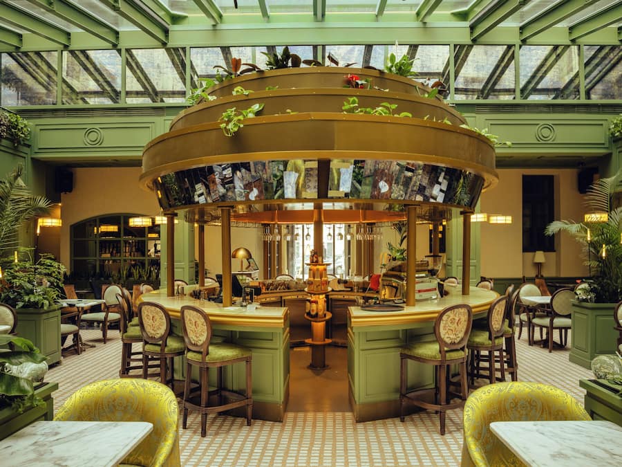 A spacious, well-lit atrium with a central bar area, surrounded by seating and greenery.