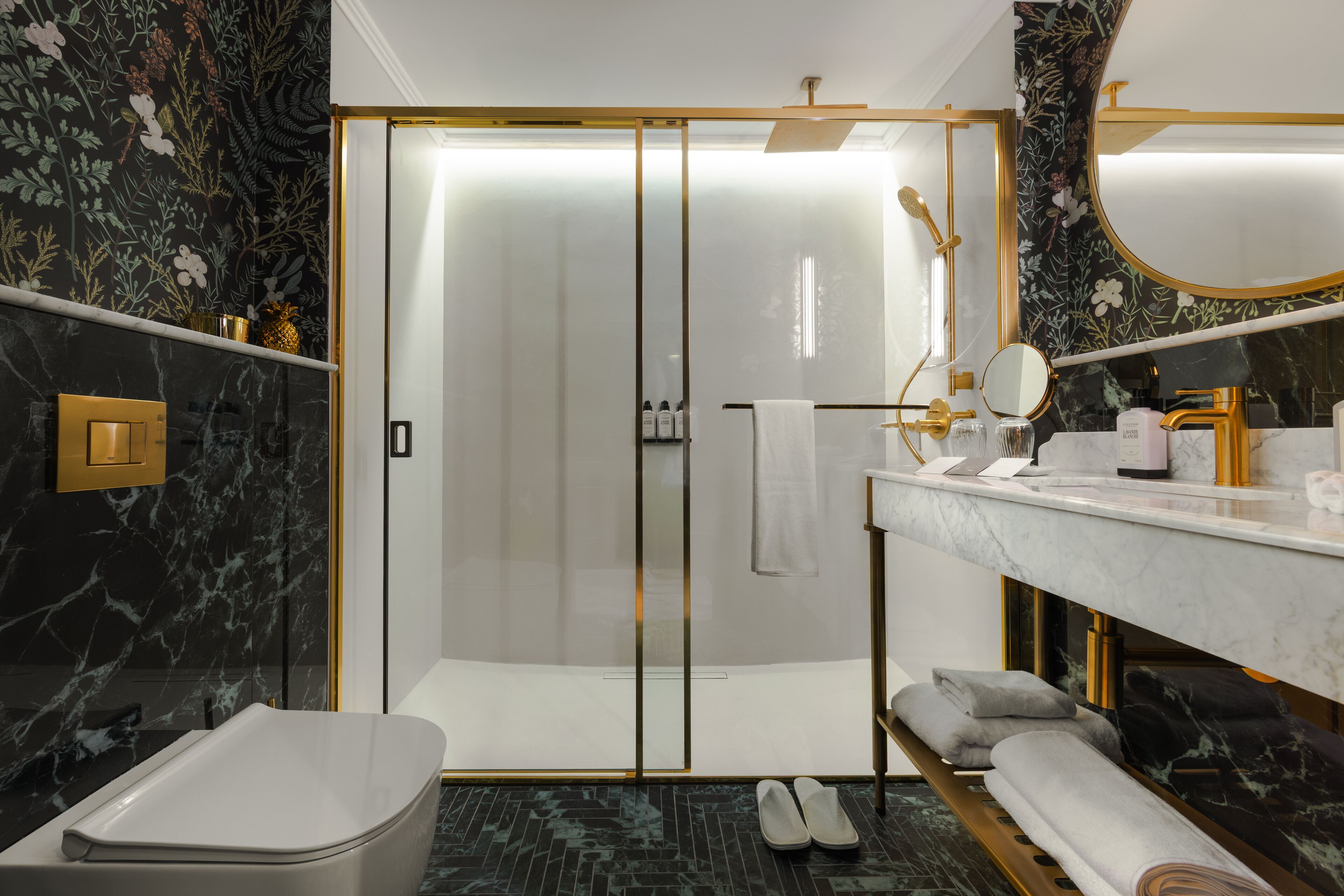Un baño moderno con ducha de vidrio, lavamanos de mármol y tocador con artículos de aseo.