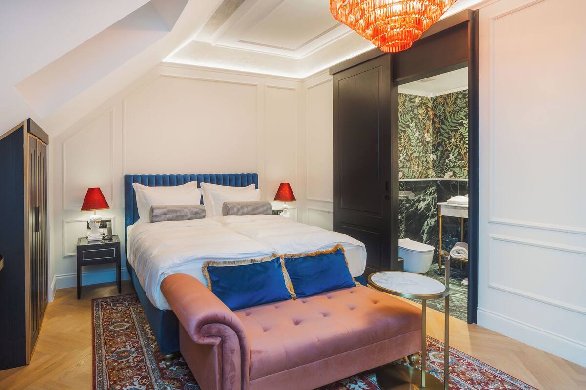 A bedroom with a large bed, two bedside tables, a pink sofa, a small round table, and a large mirror.