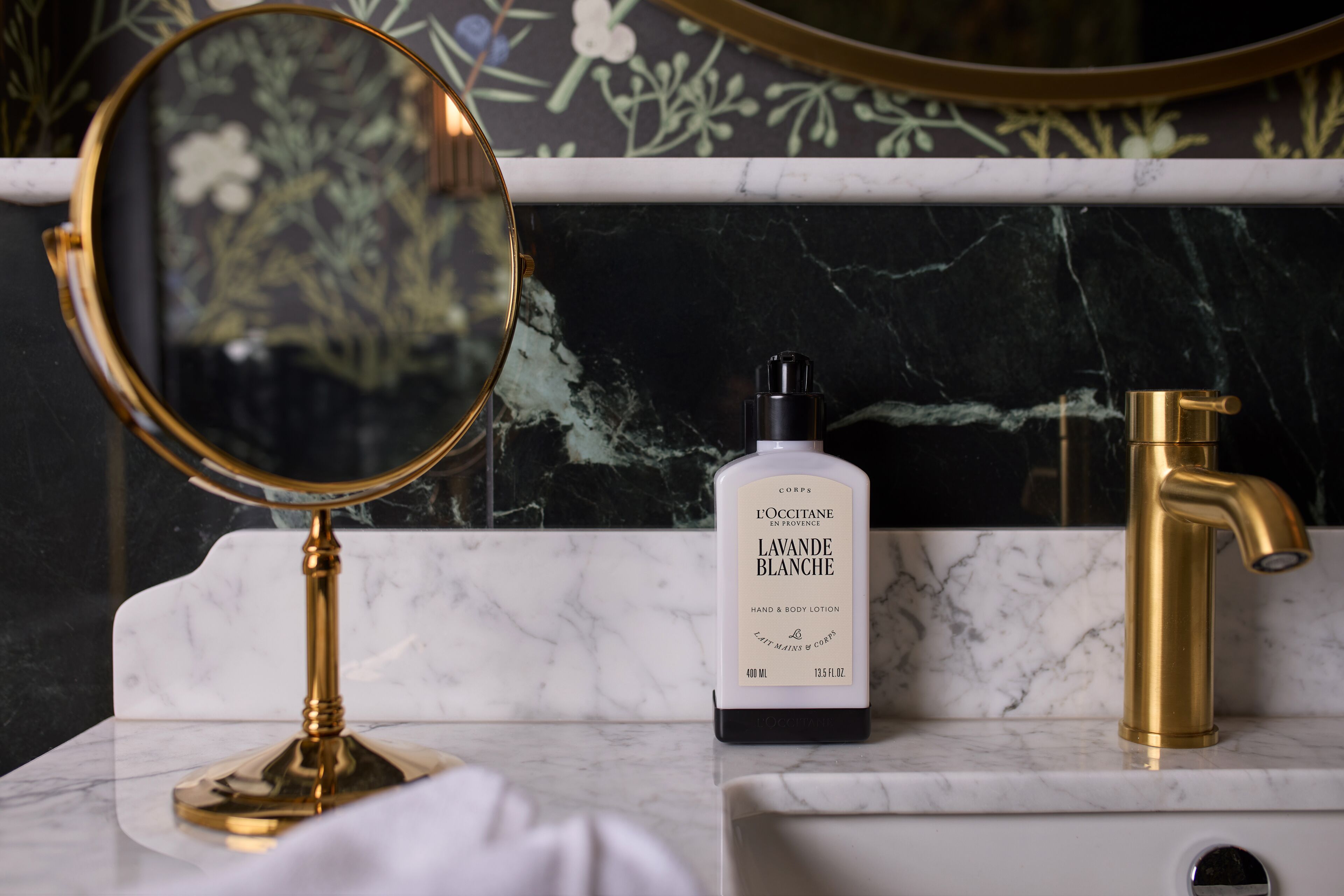 A bathroom vanity with a gold-framed mirror, a bottle of LAVANDE BLANCHE hand and body lotion, and a gold faucet.
