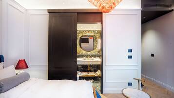 Un dormitorio con cama, mesita de noche, lámpara roja, mesa redonda y vestidor con espejo y estantes.