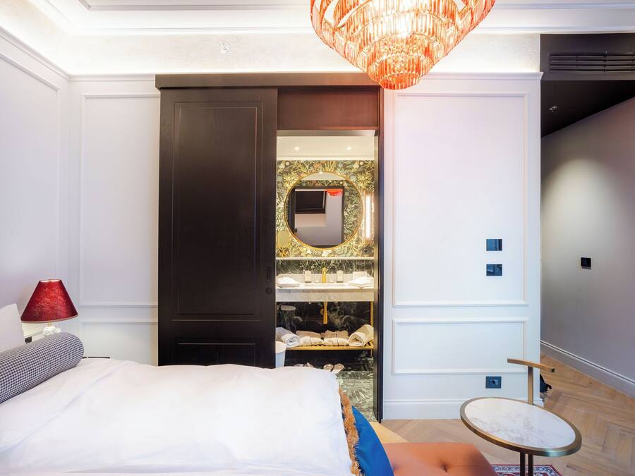 Un dormitorio con cama, mesita de noche, lámpara roja, mesa redonda y vestidor con espejo y estantes.