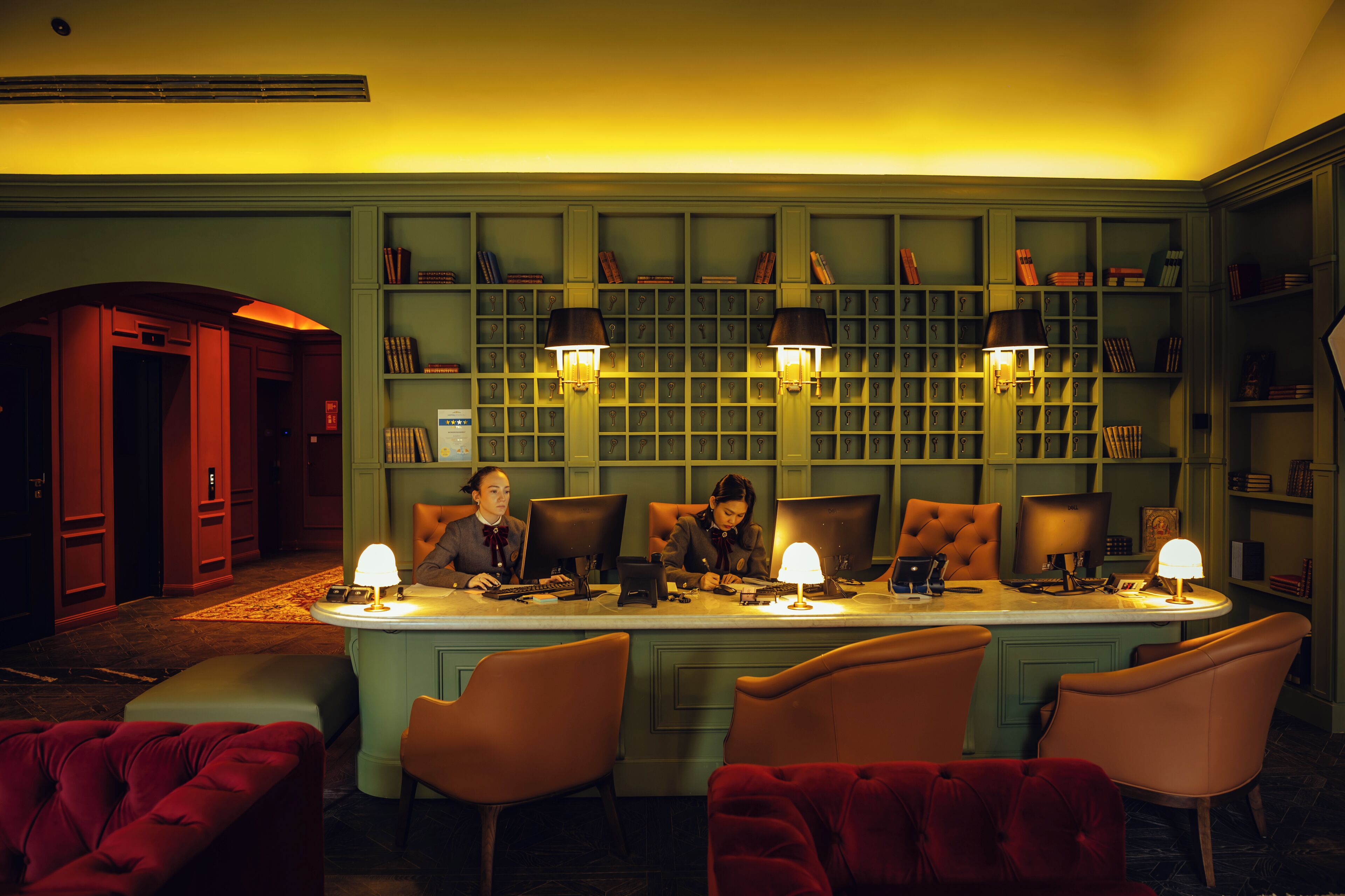 A room with a long table, four chairs, and two lamps. There are bookshelves in the background.